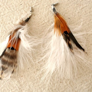 May include: A pair of feather earrings with white and brown feathers. The earrings have a silver tone metal finding.
