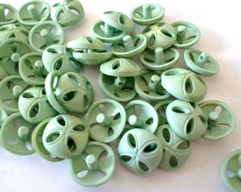 May include: A pile of light green plastic buttons with four holes and a raised center. The buttons have a decorative design with a four-leaf clover shape.