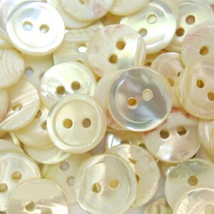 May include: A pile of white pearl-like buttons with two holes each. The buttons are smooth and shiny.