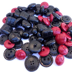 Può includere: Una collezione di bottoni in pelle nera e rossa. I bottoni sono di varie forme e dimensioni, alcuni con un bordo cucito.