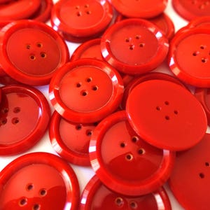以下が含まれることがあります： 鮮やかな赤色のボタンのコレクション。各ボタンには4つの穴があります。ボタンは丸く、縁がわずかに盛り上がっており、光沢のある仕上がりです。これらの裁縫用品は、さまざまなクラフトプロジェクトに最適です。