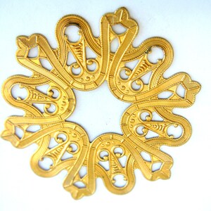 May include: A gold-colored metal decorative piece with a circular design featuring intricate swirls and curves.
