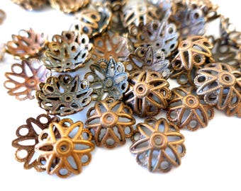 May include: A collection of antique bronze-colored filigree bead caps. The caps have a floral design with openwork details. The caps are in various shades of bronze and copper, with a few showing a patina.