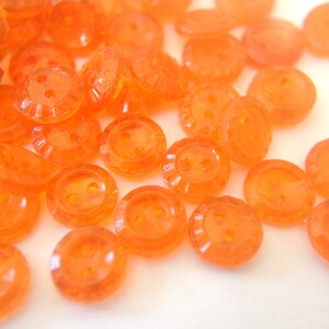 Könnte beinhalten: Eine Sammlung von orangefarbenen, zweilöchrigen Plastikknöpfen. Die Knöpfe sind durchscheinend und haben eine leicht strukturierte Oberfläche.
