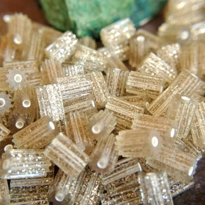 May include: A close-up of a pile of small, clear plastic gears with a glittery finish. The gears are arranged in a random pattern and are all the same size.