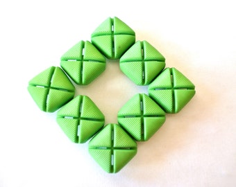 May include: Eight green, square-shaped buttons with a cross pattern on each. The buttons are arranged in a circle with a small gap in the center.