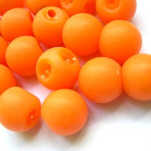 May include: A group of bright orange round beads with a smooth texture. The beads are scattered on a white surface.
