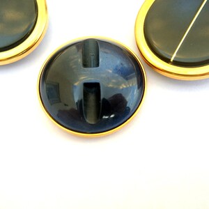 May include: Three round, black buttons with a gold rim. The center button has a vertical slit.