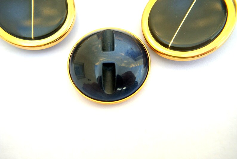 May include: Three round, black buttons with a gold rim. The center button has a vertical slit.