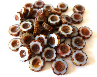 May include: A collection of flower-shaped beads. Each bead features a brown center, a white petal-like edge, and a brown rim. The beads are scattered on a white surface, creating a visually appealing arrangement. These beads are ideal for jewelry making.