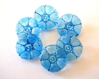 May include: Six blue glass buttons with a flower design. The buttons are round and have a raised, textured surface.