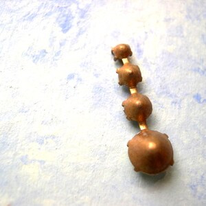 Puede incluir: Un colgante de metal dorado con cinco piedras redondas facetadas. Las piedras est&aacute;n dispuestas en l&iacute;nea vertical, con la piedra m&aacute;s grande en la parte inferior.