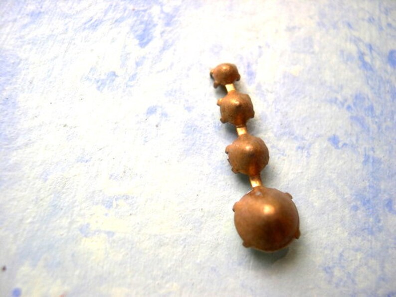 Puede incluir: Un colgante de metal dorado con cinco piedras redondas facetadas. Las piedras est&aacute;n dispuestas en l&iacute;nea vertical, con la piedra m&aacute;s grande en la parte inferior.