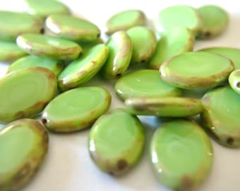 May include: A collection of oval-shaped green glass beads with a subtle iridescent sheen. The beads have a light brown swirl pattern on the surface.
