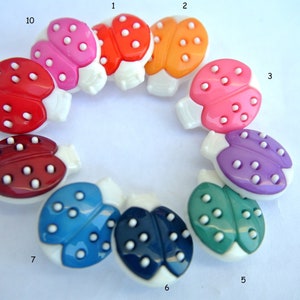 May include: A selection of ladybird-shaped buttons in a variety of colours, including red, orange, pink, purple, blue, and green. Each button has a white base and white dots. These buttons are suitable for sewing and craft projects.