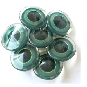 Puede incluir: Un grupo de siete botones de vidrio verde con círculos concéntricos negros y blancos. Los botones son redondos y tienen un acabado brillante.