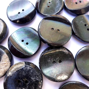 May include: A collection of black and green iridescent buttons with two holes each. The buttons are made of a smooth, shiny material and have a slightly rounded shape.