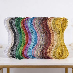 May include: A collection of colorful embroidery floss in various shades, including white, black, green, red, purple, blue, brown, and gold. The floss is neatly arranged, showcasing a spectrum of hues for crafting projects.