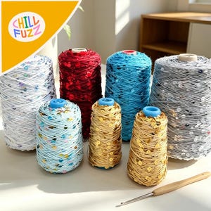 May include: A collection of colorful yarn spools with sequins. The spools are in various colors, including red, blue, gold, and silver. A crochet hook with a wooden handle is also present. The logo "CHILL FUZZ" is in the upper left corner.