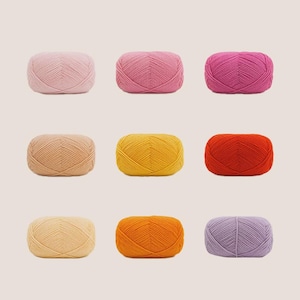 May include: Nine skeins of yarn in various colors, including pink, tan, yellow, orange, red, and purple. The yarn is arranged in three rows of three, each skein neatly wound and ready for crafting projects.