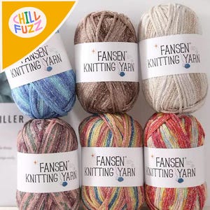 Puede incluir: Seis madejas de hilo para tejer FANSEN en varios colores. Los colores del hilo incluyen azul, marrón, beige, rosa, arcoíris y rojo. Cada madeja tiene una etiqueta blanca con el nombre de la marca y "Knitting Yarn" impreso. La esquina superior izquierda tiene un logotipo amarillo y naranja con las palabras "CHILL FUZZ".
