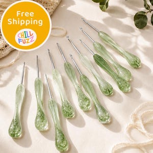 Può includere: Un set di nove uncinetti con aste metalliche e manici in resina traslucida verde chiaro con motivi vorticosi interni. I manici presentano un design ergonomico, liscio e a forma di goccia, mentre gli uncini metallici variano nelle dimensioni.