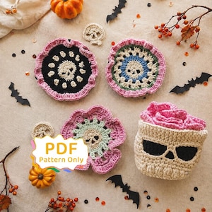 Könnte beinhalten: Drei runde Häkeluntersetzer mit Totenkopfmotiven in Schwarz, Blau und Hellgrün mit rosa gerüschten Rändern sowie ein beiger Häkelkorb in Totenkopfform mit rosa gerüschtem Rand. Ein weißes Etikett mit dem Text PDF Pattern Only ist zu sehen.