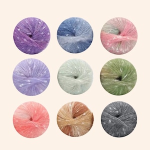 May include: Nine balls of colorful yarn in a variety of colors, including purple, blue, pink, lavender, green, orange, tan, and gray. Each ball is speckled with white dots, and the yarn appears soft and fluffy. The yarn is arranged in a grid pattern.