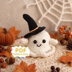 May include: A white crocheted ghost figure wearing a black witch hat with an orange band, featuring black plastic eyes and a stitched smile. A white label with the text PDF Pattern Only is positioned in the lower left corner of the image.