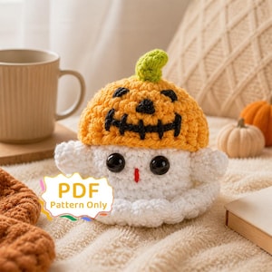 May include: A white crocheted ghost plushie wearing a bright orange pumpkin hat with a green stem and a black stitched jack-o'-lantern face. The ghost has large black safety eyes and a small red stitched mouth. A label reads PDF Pattern Only.
