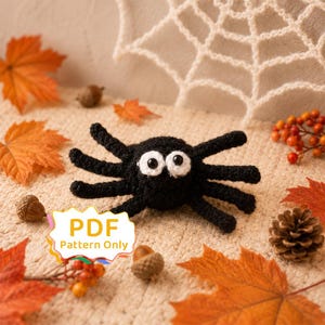 May include: A black crocheted spider toy with two large white-rimmed eyes. The spider has eight legs and a round body. A white label with a colorful border displays the text PDF Pattern Only in the lower left corner of the image.