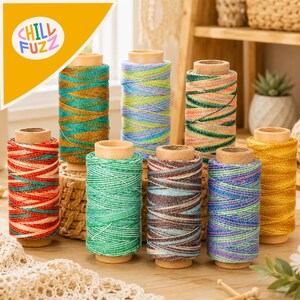 May include: A collection of eight cylindrical spools of metallic embroidery thread in various vibrant colors including teal, gold, green, blue, and coral. Each spool features a cardboard core and a distinct multi-colored, shimmering thread pattern.