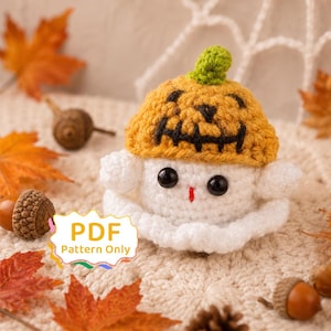 May include: A white crocheted ghost figure wearing a yellow pumpkin hat with a black stitched jack-o'-lantern face, featuring two black plastic eyes and a small red stitched mouth. A white label with the text PDF Pattern Only is visible.