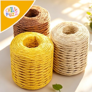 Puede incluir: Tres carretes de hilo en tonos amarillo, marrón y beige. El carrete amarillo está en primer plano, con los carretes marrón y beige detrás. El logotipo "CHILL FUZZ" está en la esquina superior izquierda.