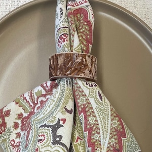 May include: A brown and white paisley patterned napkin ring with a brown wooden napkin ring.