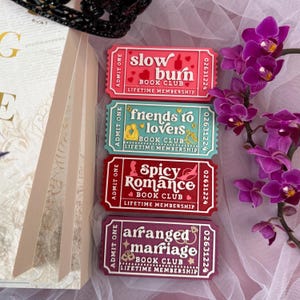 K&ouml;nnte beinhalten: Vier farbenfrohe Magnete in Form von Buchclub-Tickets. Die Magnete zeigen die S&auml;tze "slow burn", "friends to lovers", "spicy romance" und "arranged marriage". Jeder Magnet hat ein einzigartiges Farbschema und Design mit den Worten "book club" und "lifetime membership".