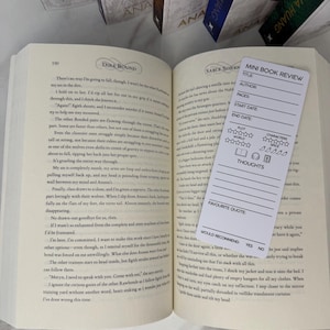 Op de afbeelding: Een open boek met tekst op de pagina's en een witte mini-boekrecensie-bladwijzer. De bladwijzer heeft secties voor titel, auteur, pagina's, start- en einddatum, plot, wereld, personages, spice, gedachten en favoriete citaat.