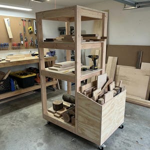 Puede incluir: Un carro de almacenamiento de madera de madera con múltiples estantes y un contenedor. El carro está lleno de piezas de madera de varios tamaños, incluyendo tablones, bloques y troncos. Un taladro inalámbrico y una cinta métrica están en un estante.