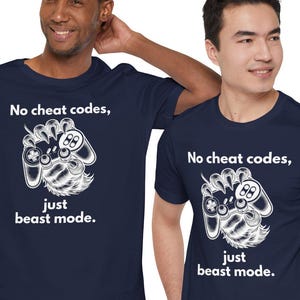 Puede incluir: Dos camisetas azul marino con un gráfico blanco de una mano sosteniendo un mando de videojuego. El texto en las camisetas dice "No cheat codes, just beast mode."
