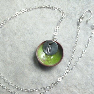 May include: A silver chain necklace with a green and red enamel pendant. The pendant has a silver disc with the letter "W" on it.