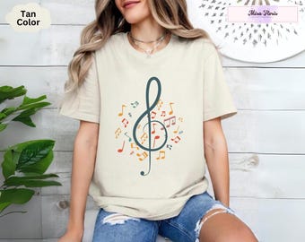 May include: A tan t-shirt featuring a graphic of a treble clef surrounded by musical notes in various colours. The notes are in shades of red, orange, yellow, green, blue, and purple.