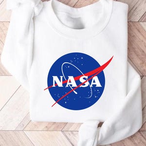 May include: White sweatshirt with a blue and red NASA logo printed on the front.