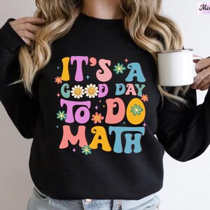 May include: Black sweatshirt with a colorful graphic that says "It's a good day to do math". The graphic features flowers, smiley faces, and a rainbow.