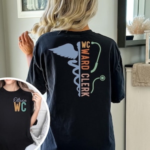 May include: Black t-shirt with a colorful graphic of a medical caduceus and the text "WC Ward Clerk". The text is in a vertical orientation. The t-shirt has a crew neck and short sleeves.