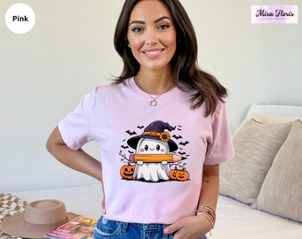 May include: Pink t-shirt featuring a cartoon ghost wearing a witch hat and holding a pencil. The design includes pumpkins, bats, and a sunflower. The shirt has the Mira Floris logo in the upper right corner.