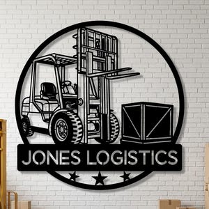 Puede incluir: Arte de pared de metal negro con una carretilla elevadora dentro de un círculo, con el texto "JONES LOGISTICS" debajo. El diseño incluye estrellas y una caja. Una carretilla elevadora amarilla y cajas de cartón en primer plano.