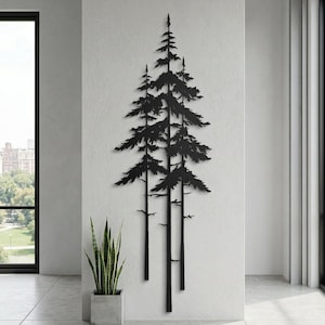 May include: Black metal wall art depicting a stylized forest scene with three tall pine trees. The artwork is mounted on a white wall in a modern interior setting, with a potted plant in the foreground.