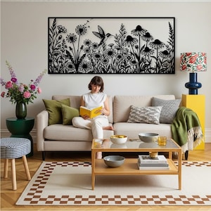 May include: A rectangular black metal wall art piece featuring a detailed silhouette of a hummingbird hovering among various wildflowers and dandelion seed heads. The design is intricate, showcasing stems, leaves, and flower petals in a flat, dark finish.