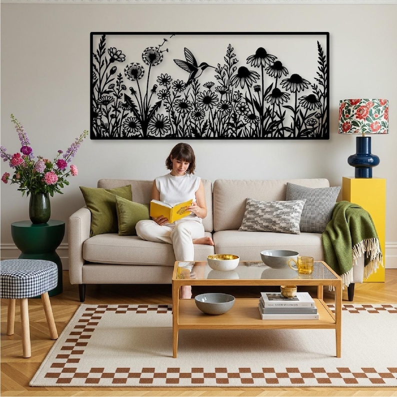 May include: A rectangular black metal wall art piece featuring a detailed silhouette of a hummingbird hovering among various wildflowers and dandelion seed heads. The design is intricate, showcasing stems, leaves, and flower petals in a flat, dark finish.