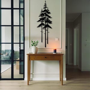 May include: A wooden console table with a drawer and a white vase with greenery on top. A black metal tree silhouette hangs on the wall above the table. A lit candle sits on the table, adding a warm glow to the room.